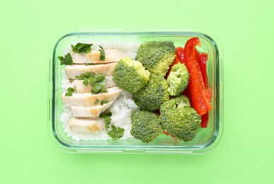 Photo of Healthy meal. Fresh broccoli, pepper, chicken and rice in glass container on green background, top view