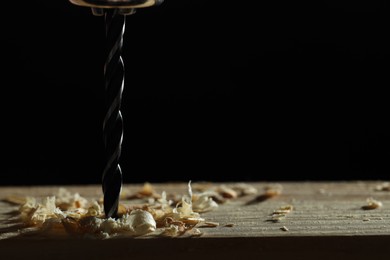 Electric drill and sawdust on black background, closeup. Space for text