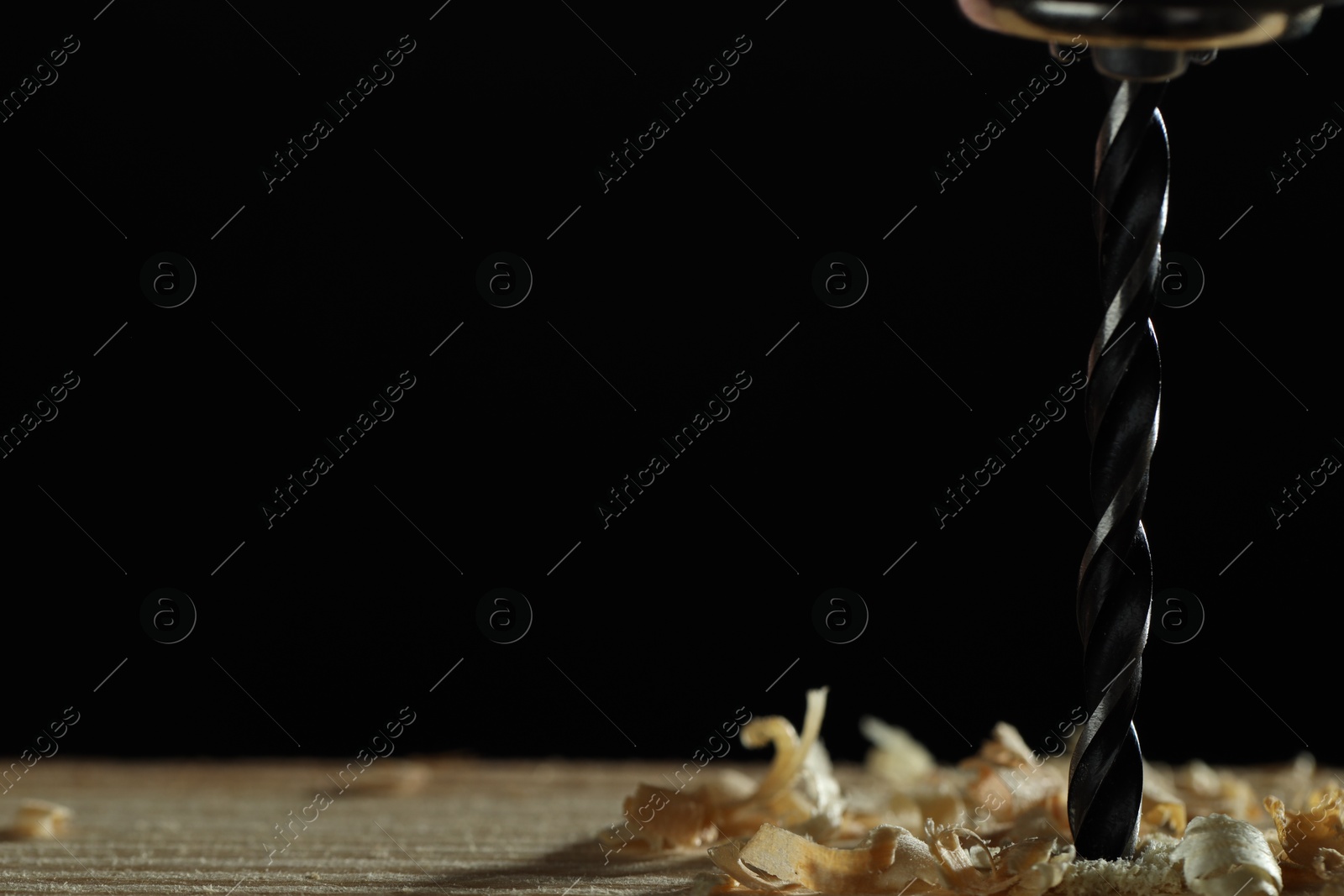 Photo of Electric drill and sawdust on black background, closeup. Space for text