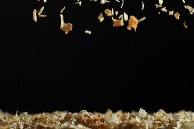 Photo of Dry natural sawdust falling on black background, space for text