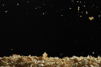 Dry natural sawdust falling on black background, space for text