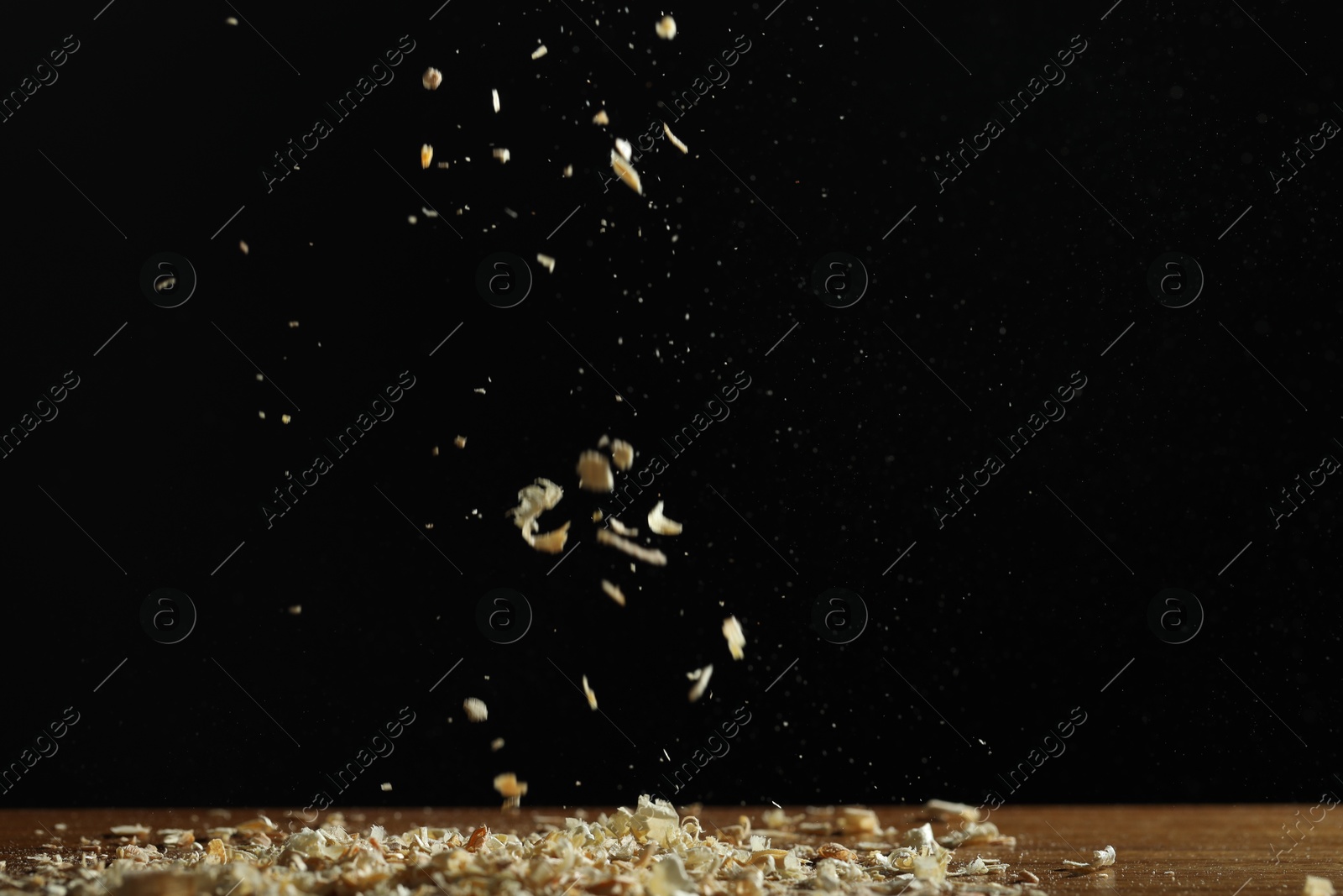 Photo of Dry natural sawdust falling on table against black background, space for text