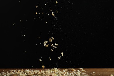 Dry natural sawdust falling on table against black background, space for text