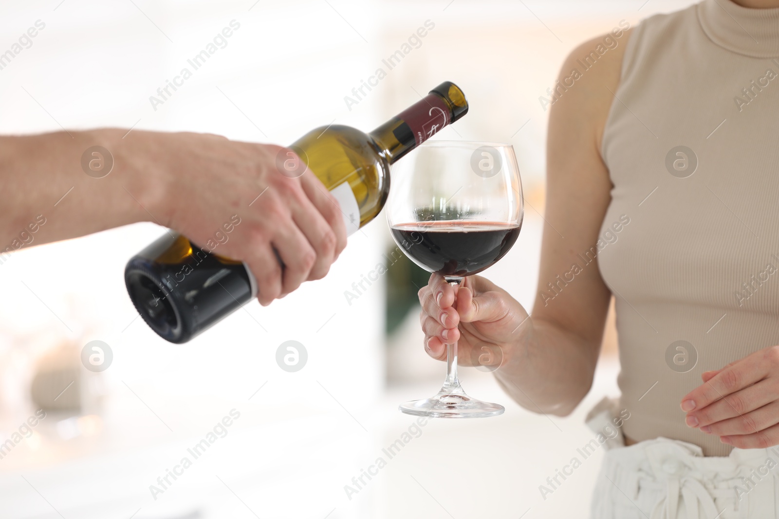 Photo of Man pouring red wine into woman`s glass indoors, closeup