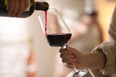 Man pouring red wine into woman`s glass indoors, selective focus