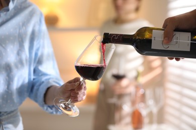 Photo of Man pouring red wine into woman`s glass indoors, selective focus