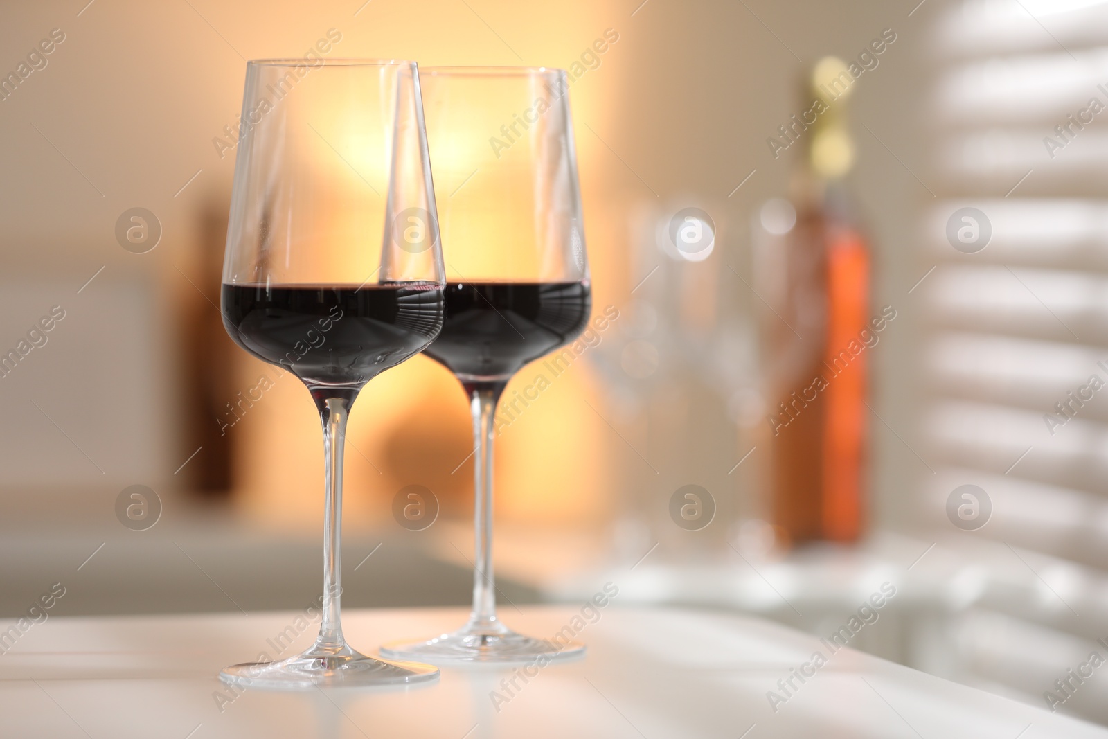 Photo of Red wine in glasses on white table against blurred background, space for text