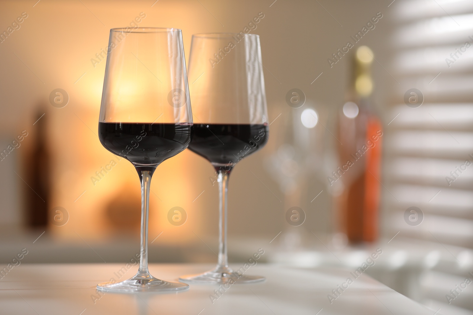 Photo of Red wine in glasses on white table against blurred background, space for text