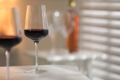 Photo of Red wine in glasses on white table against blurred background, space for text