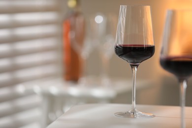 Red wine in glasses on white table against blurred background, space for text