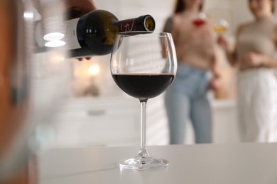 Photo of Man pouring red wine into glass at white table, selective focus