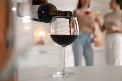 Man pouring red wine into glass at white table, selective focus