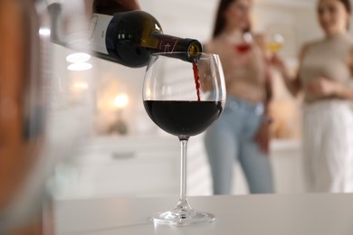Man pouring red wine into glass at white table, selective focus