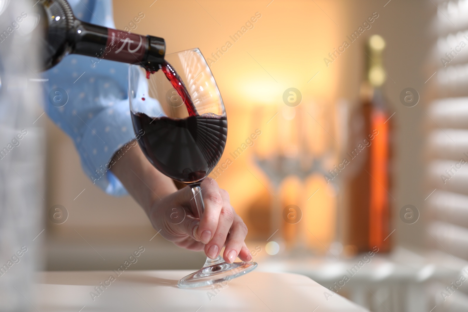 Photo of Woman pouring red wine into glass at white table indoors, closeup. Space for text