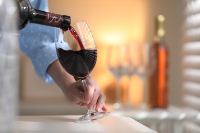 Photo of Woman pouring red wine into glass at white table indoors, closeup. Space for text