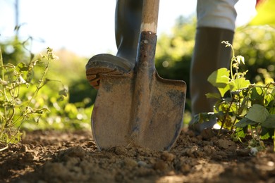 Photo of Farmer digging soil with shovel on sunny day, closeup