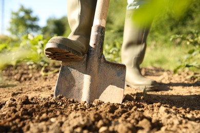 Photo of Farmer digging soil with shovel on sunny day, closeup