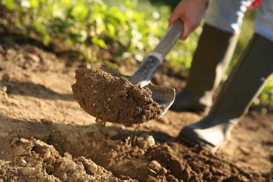 Photo of Farmer digging soil with shovel on sunny day, closeup