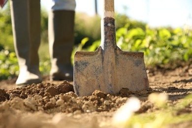 Photo of Farmer digging soil with shovel on sunny day, closeup