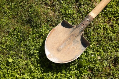 Photo of One rusty shovel on green grass, top view. Gardening season