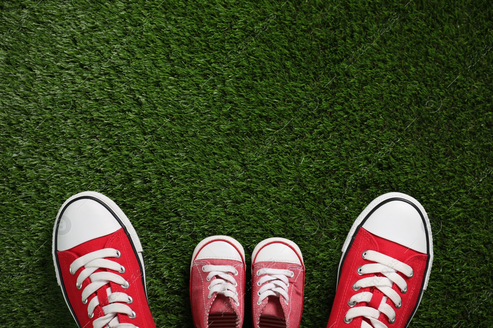 Photo of Big and small shoes on green grass, top view. Space for text