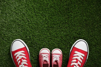 Big and small shoes on green grass, top view. Space for text