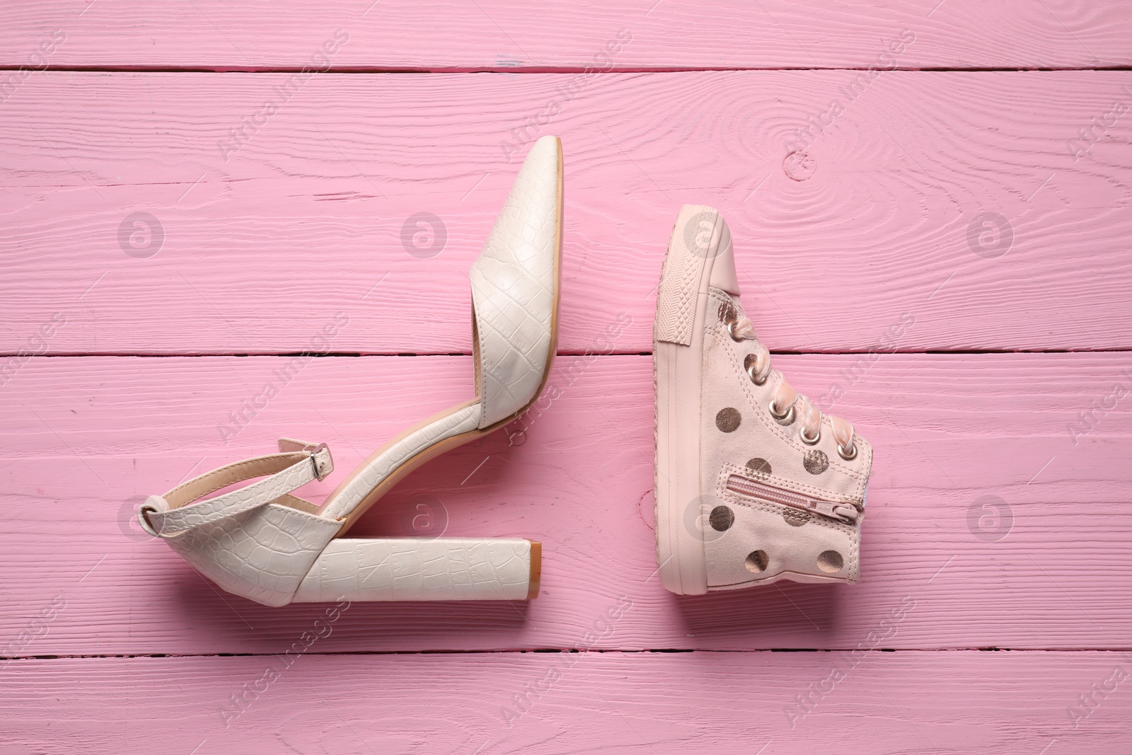 Photo of Big and small shoes on pink wooden table, top view