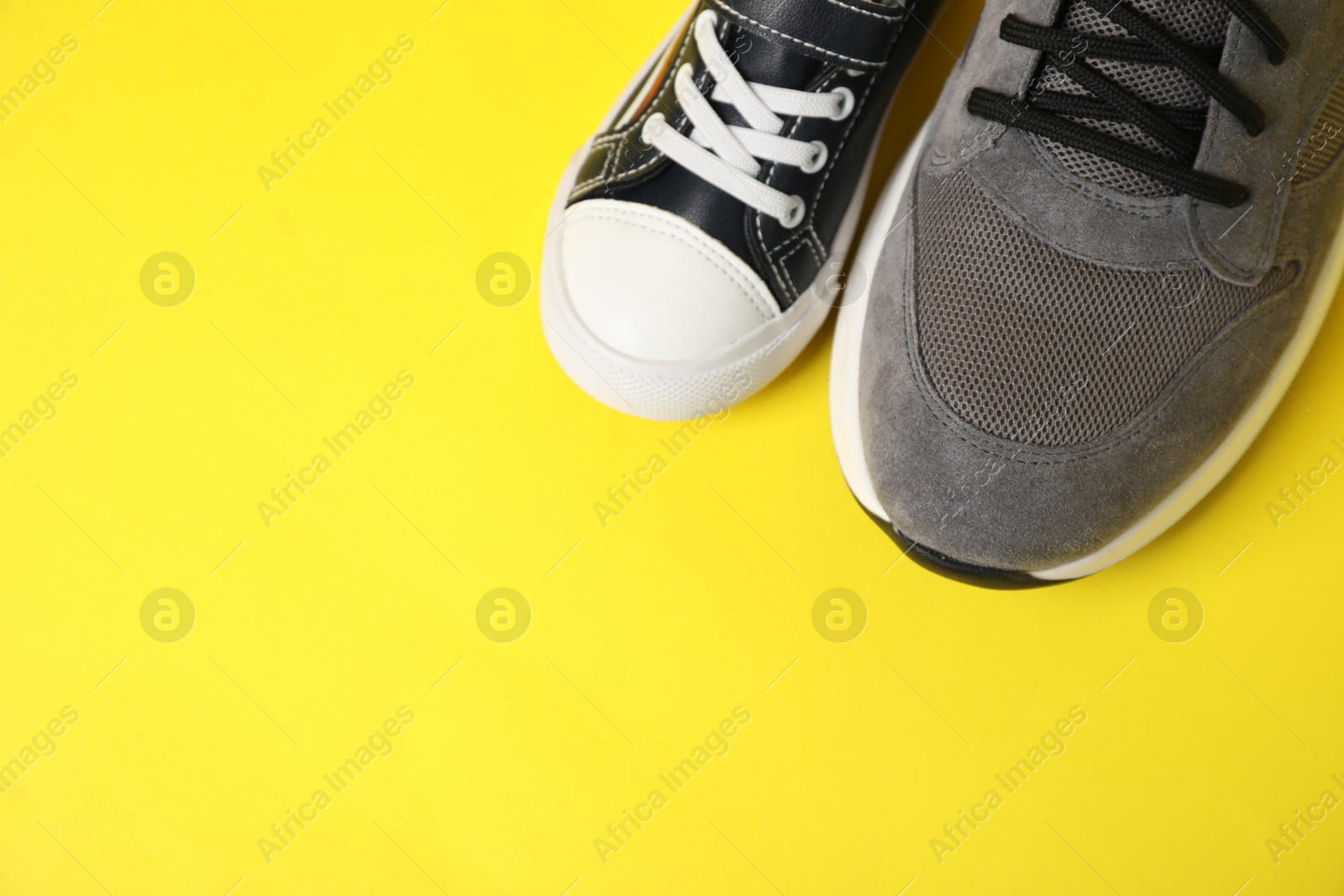 Photo of Big and small shoes on yellow background, above view. Space for text