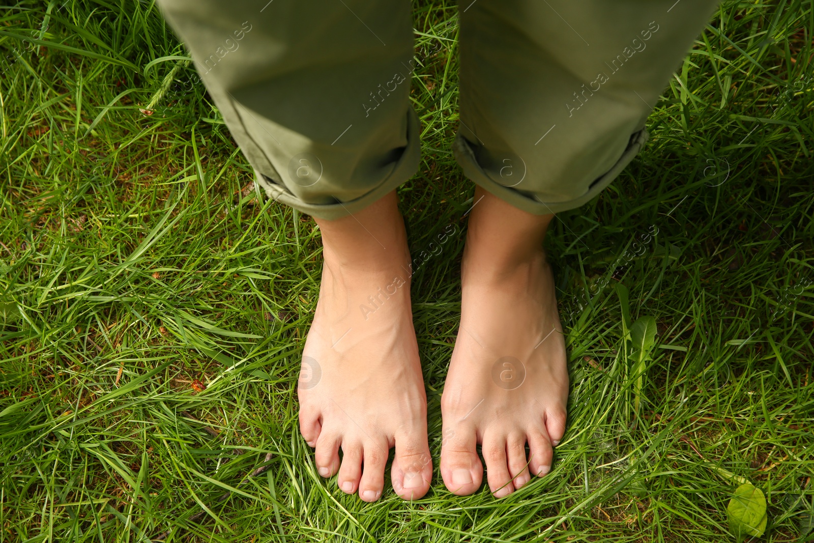 Photo of Woman walking barefoot on green grass outdoors, top view