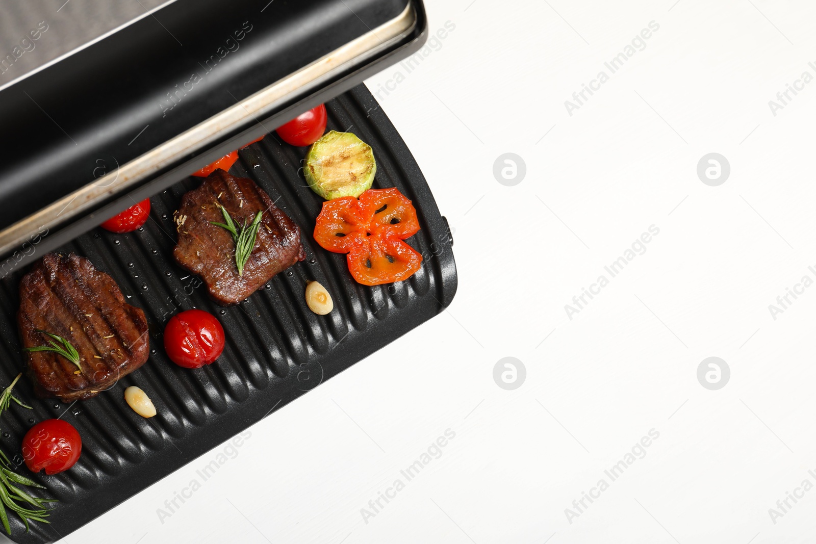 Photo of Electric grill with tasty meat, spices and vegetables on white table, top view. Space for text