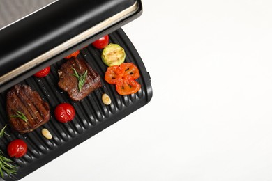 Electric grill with tasty meat, spices and vegetables on white table, top view. Space for text