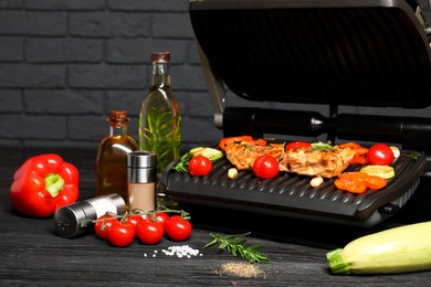 Electric grill with different products on black wooden table