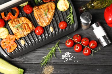 Flat lay composition with electric grill and different products on black wooden table