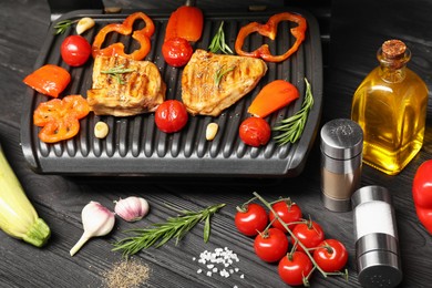 Photo of Electric grill with different products on black wooden table