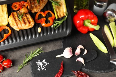 Electric grill with tasty meat, spices and vegetables on grey textured table, above view