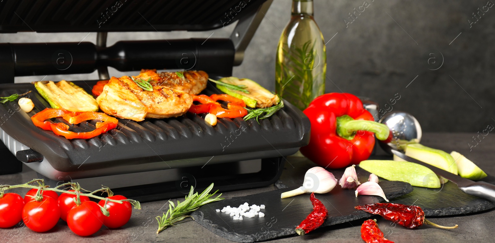 Photo of Electric grill with different products on grey textured table