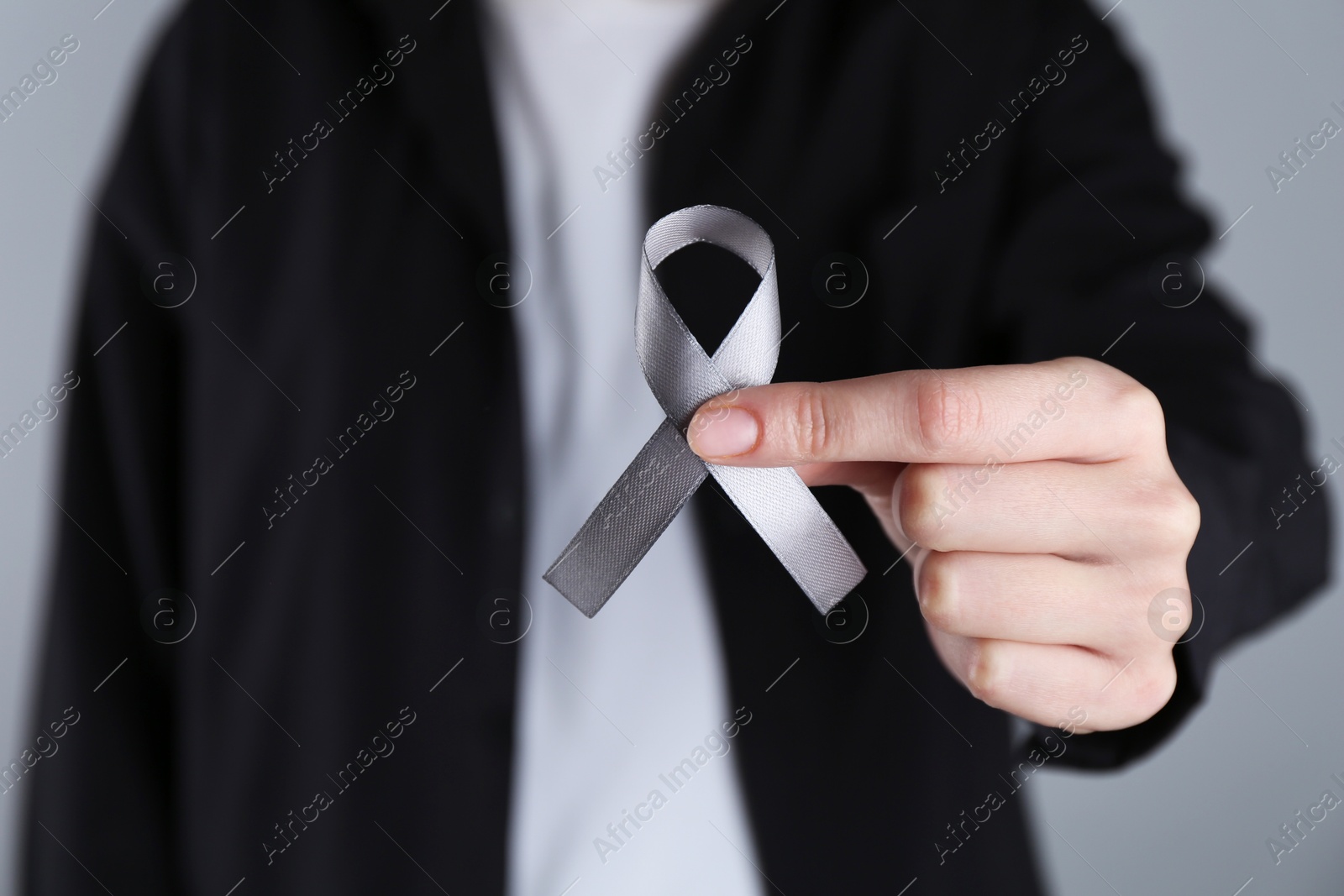 Photo of Woman holding grey awareness ribbon on color background, closeup