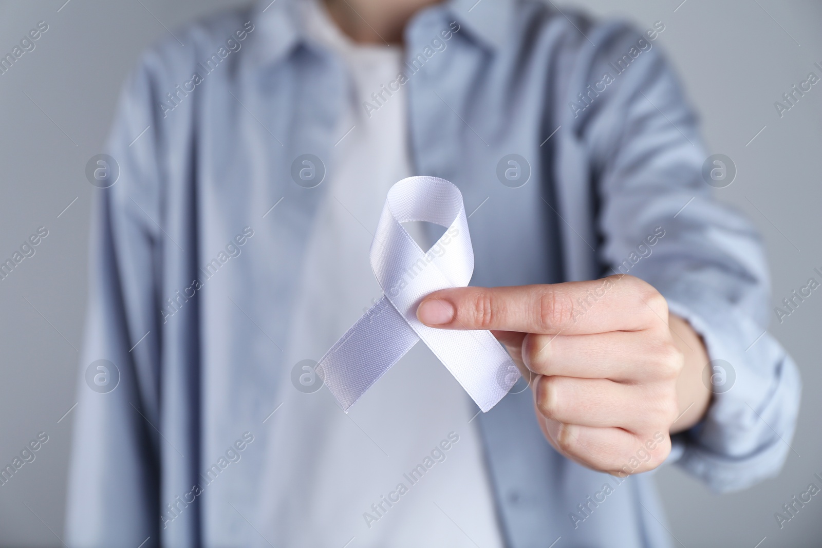 Photo of Woman holding white awareness ribbon on grey background, closeup