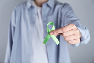 Woman with green awareness ribbon on grey background, closeup