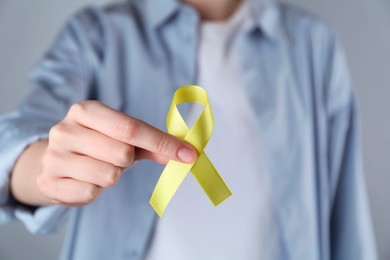 Photo of Woman with yellow awareness ribbon on grey background, closeup