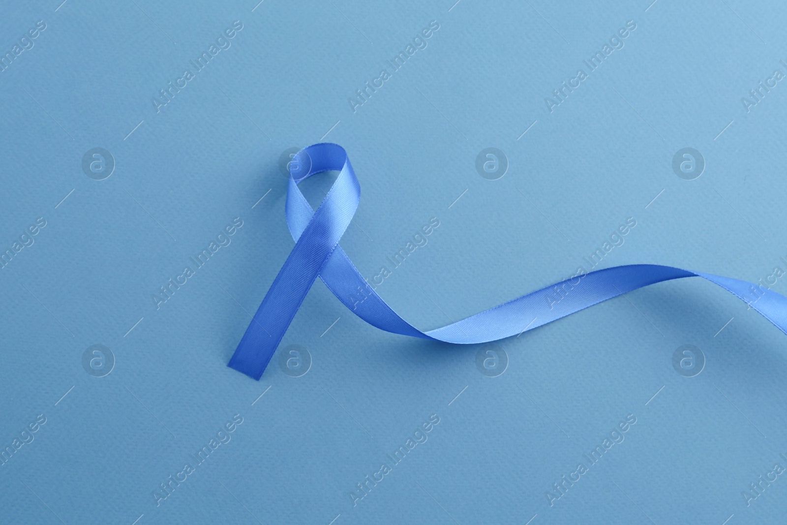 Photo of Blue awareness ribbon on color background, top view