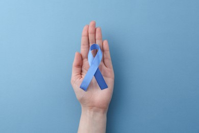 Woman with blue awareness ribbon on color background, top view