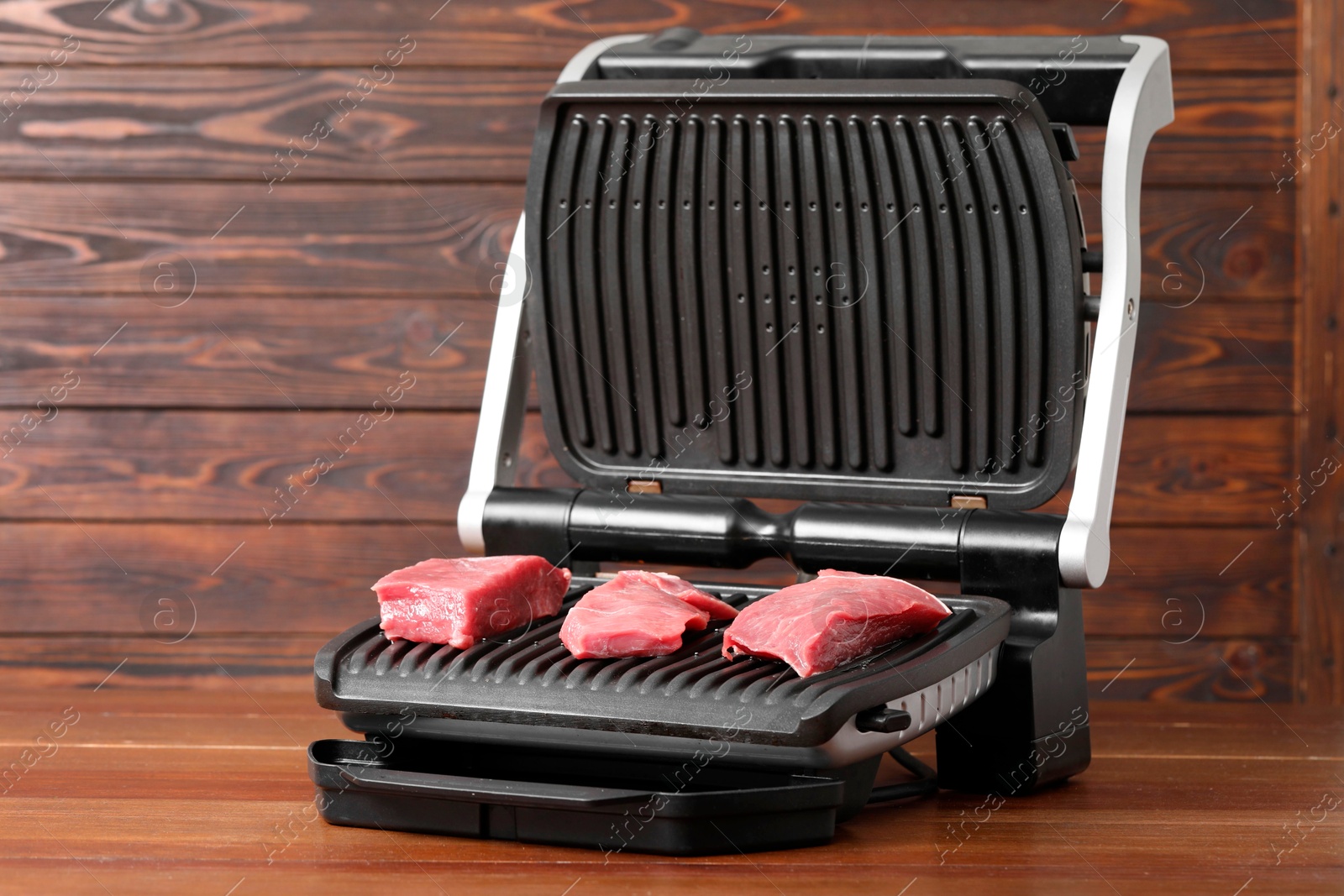 Photo of Electric grill with raw meat on wooden table