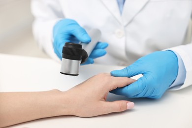 Photo of Dermatologist with dermatoscope examining patient at white table in clinic, closeup