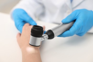 Dermatologist with dermatoscope examining patient at white table, closeup