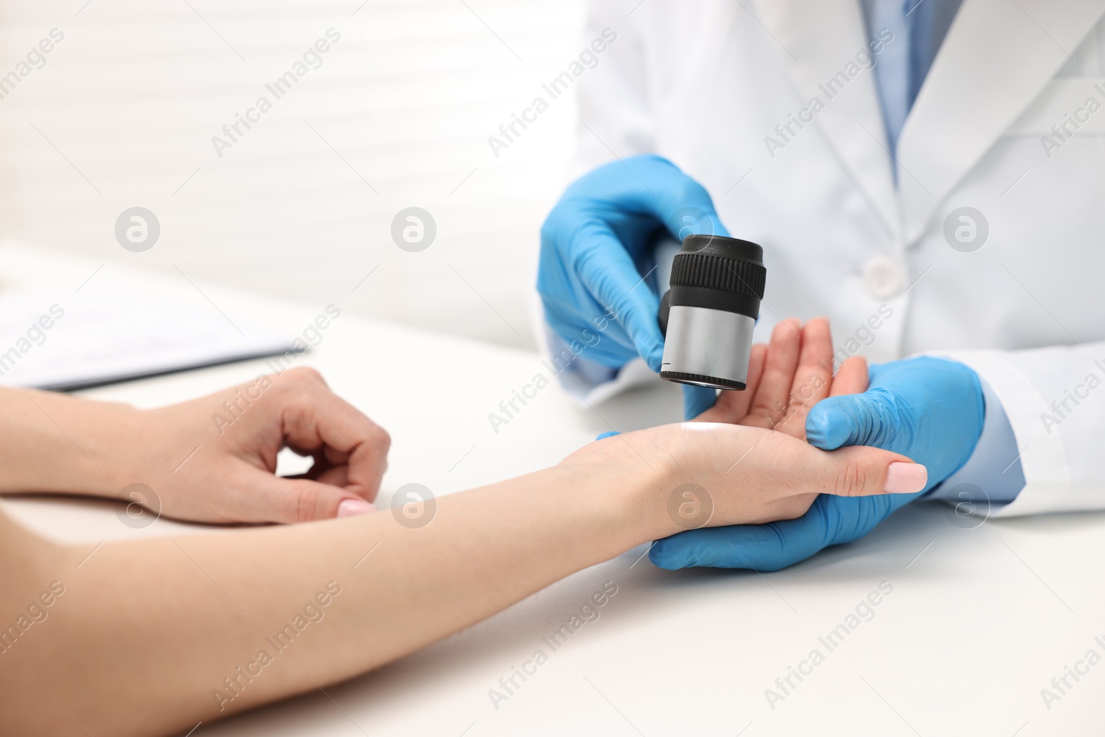Photo of Dermatologist with dermatoscope examining patient at white table in clinic, closeup