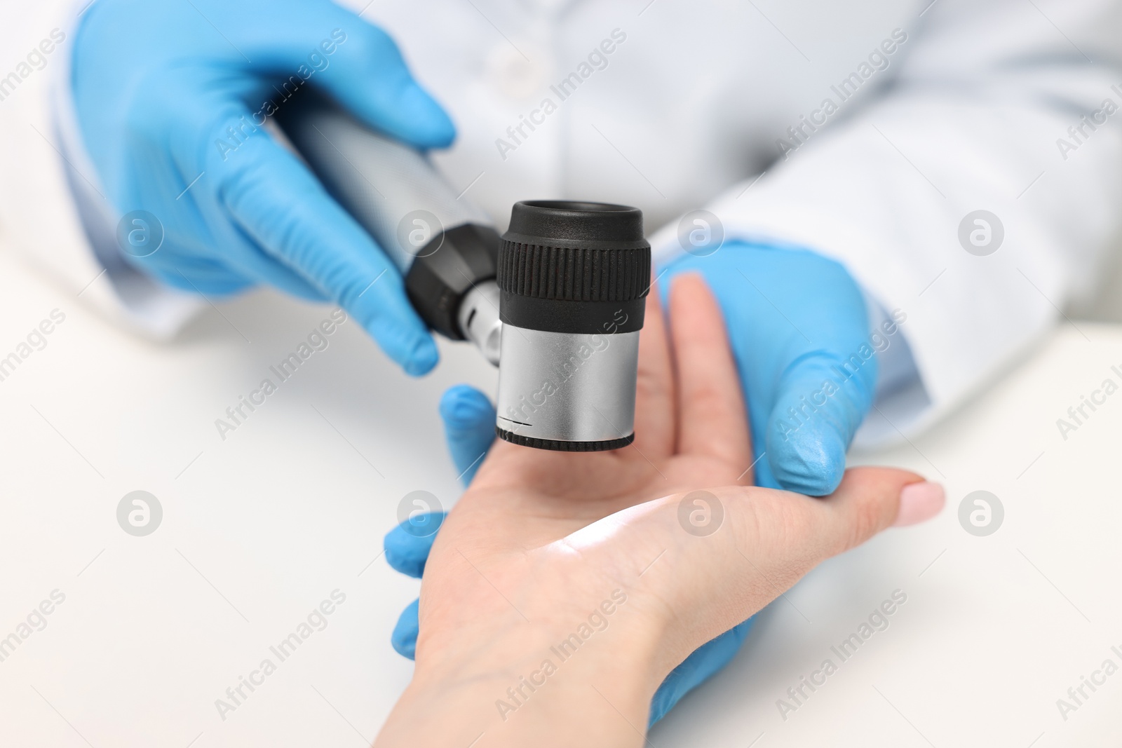 Photo of Dermatologist with dermatoscope examining patient at white table, closeup