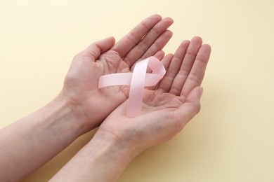 Photo of Woman with pink awareness ribbon on pale yellow background, closeup