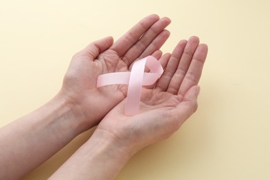 Woman with pink awareness ribbon on pale yellow background, closeup