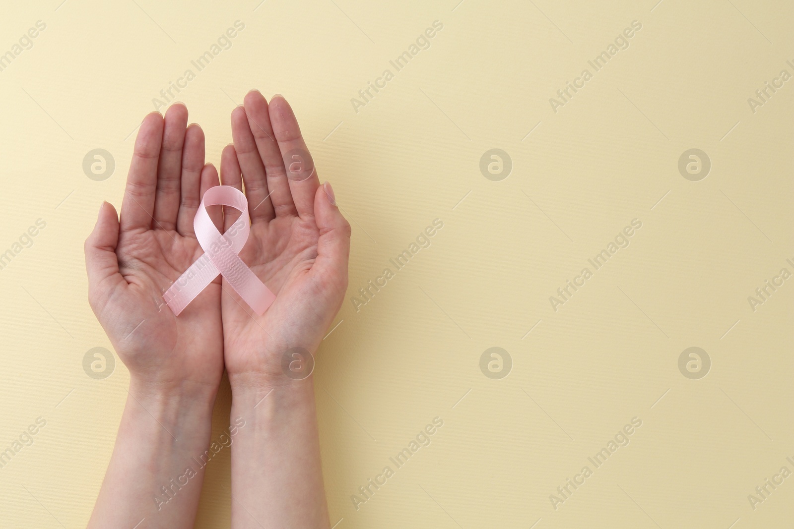 Photo of Woman with pink awareness ribbon on pale yellow background, top view. Space for text
